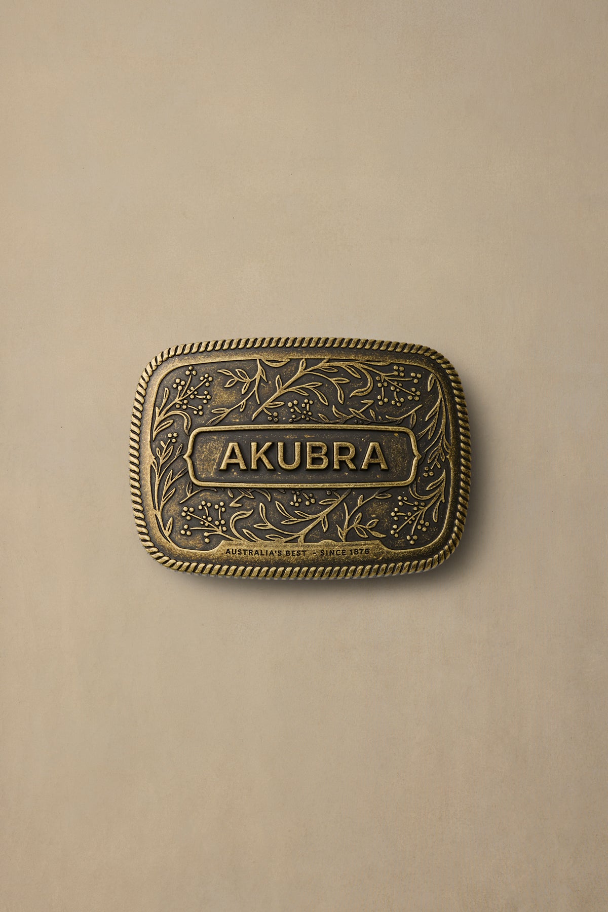 Antique brass belt buckle with ornate floral engraving and AKUBRA text on neutral background