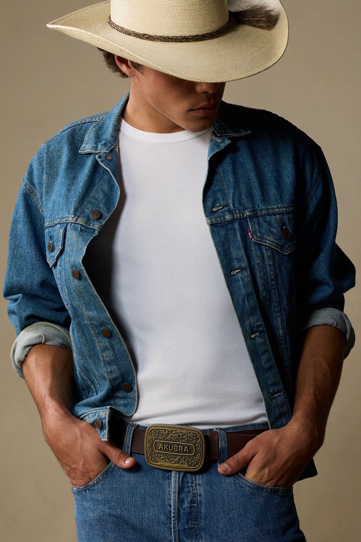 Chocolate brown leather belt with brass ornamental buckle worn with denim jacket and cowboy hat
