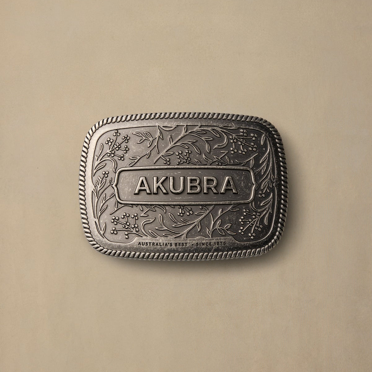 Akubra pewter belt buckle featuring ornate floral engraving and rope edge border on cream background