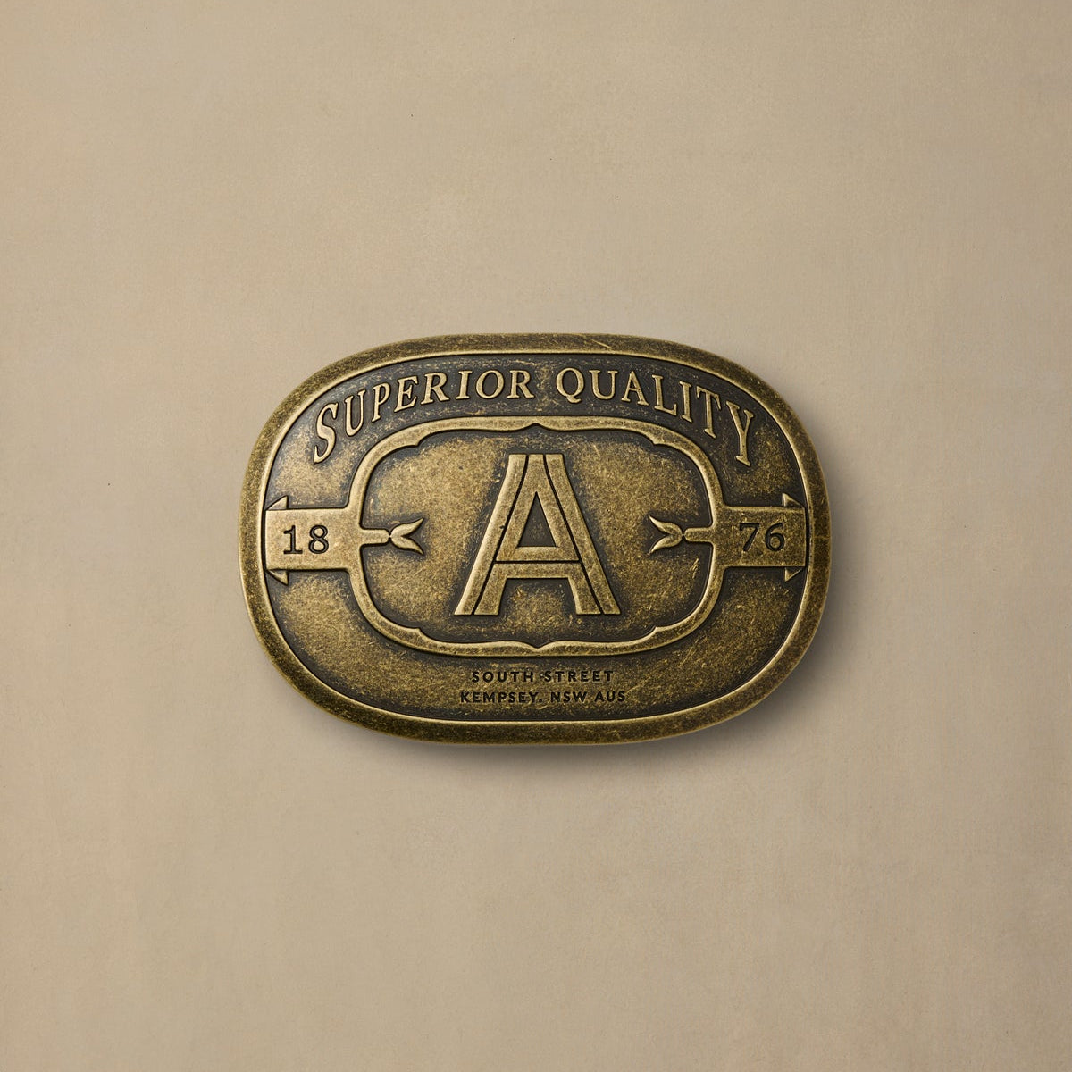 Vintage brass belt buckle with large "A" letter and "Superior Quality 1876" text on neutral background
