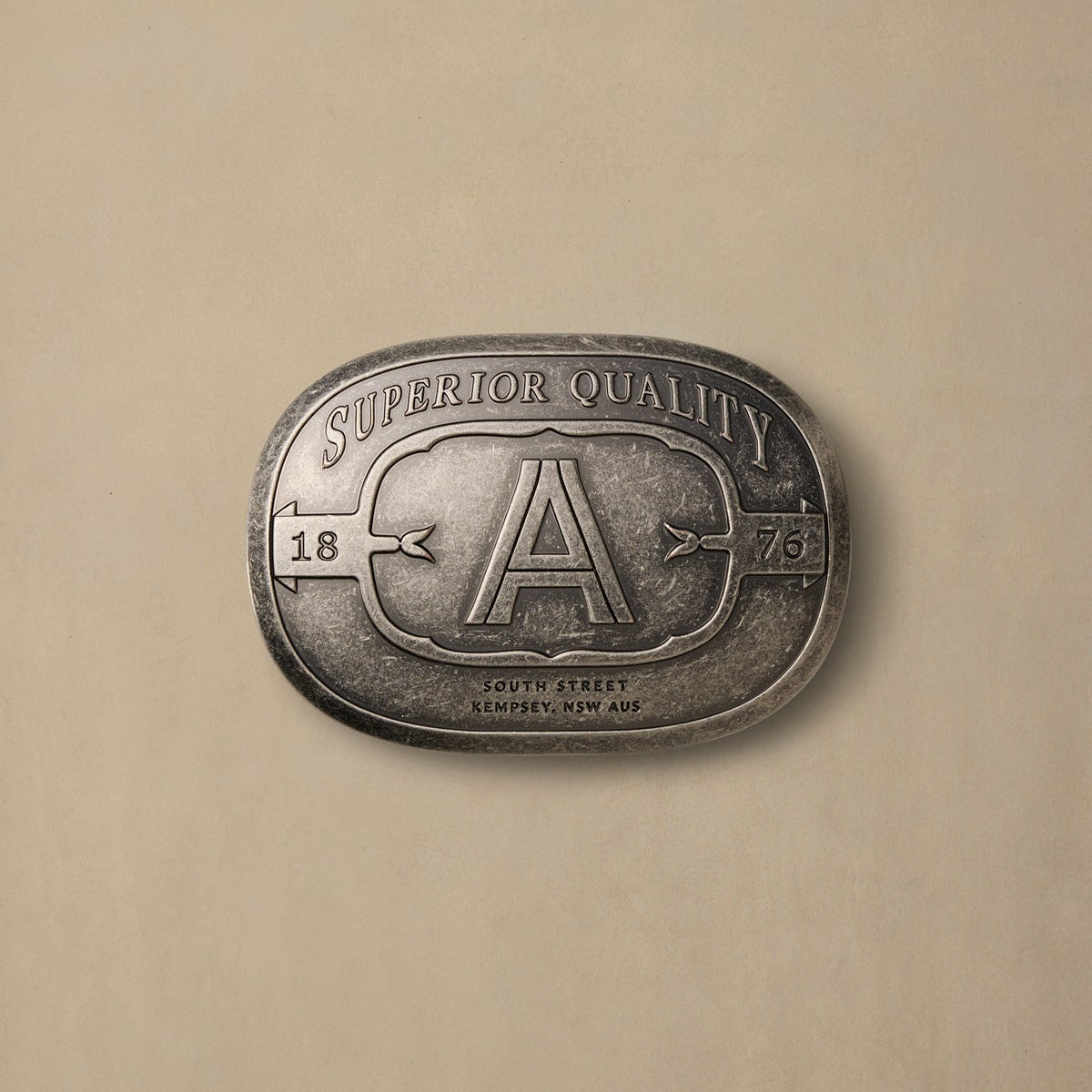 Pewter rodeo buckle with large "A" initial and superior quality text on neutral background
