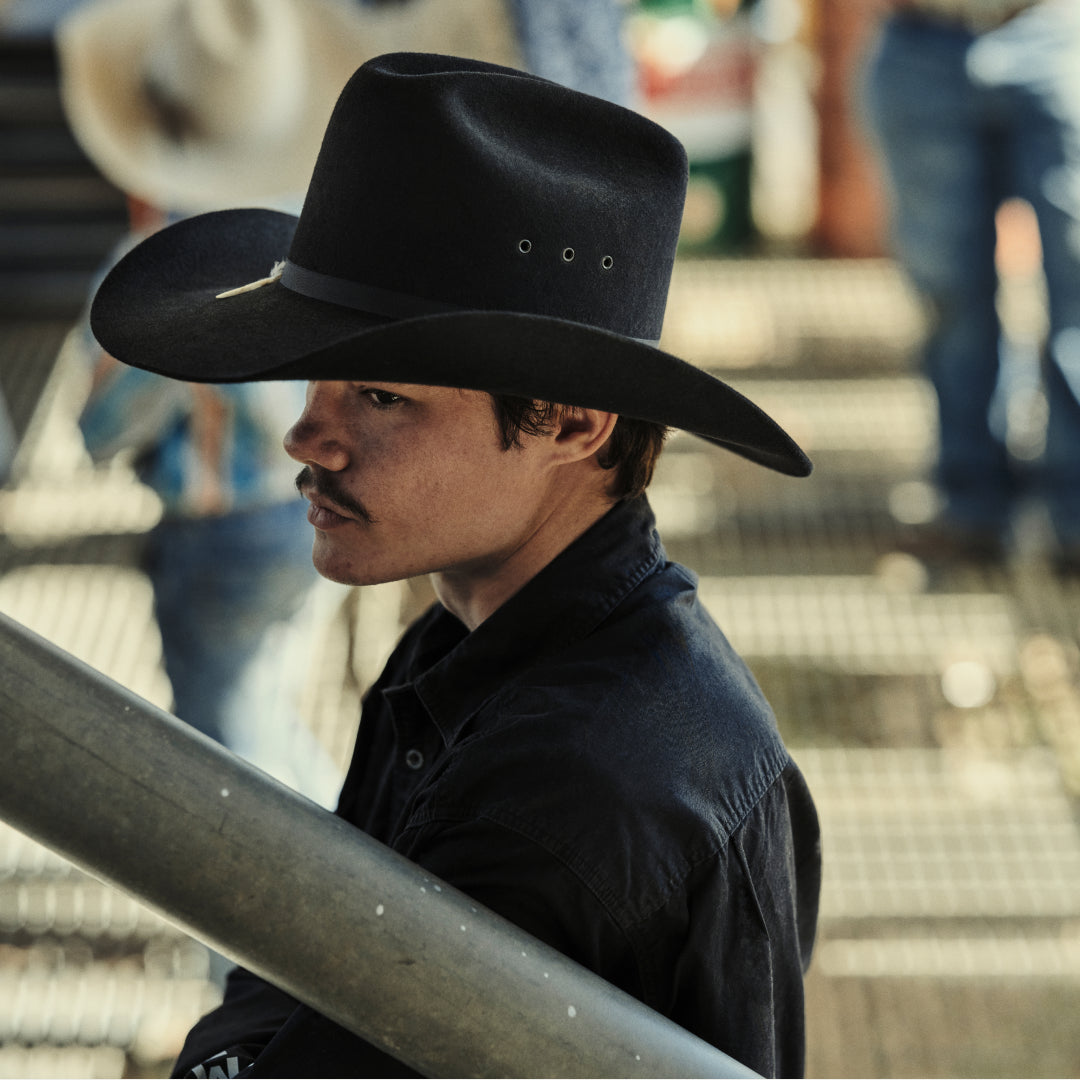 Man wearing a black cowboy hat and dark shirt on a blurred background